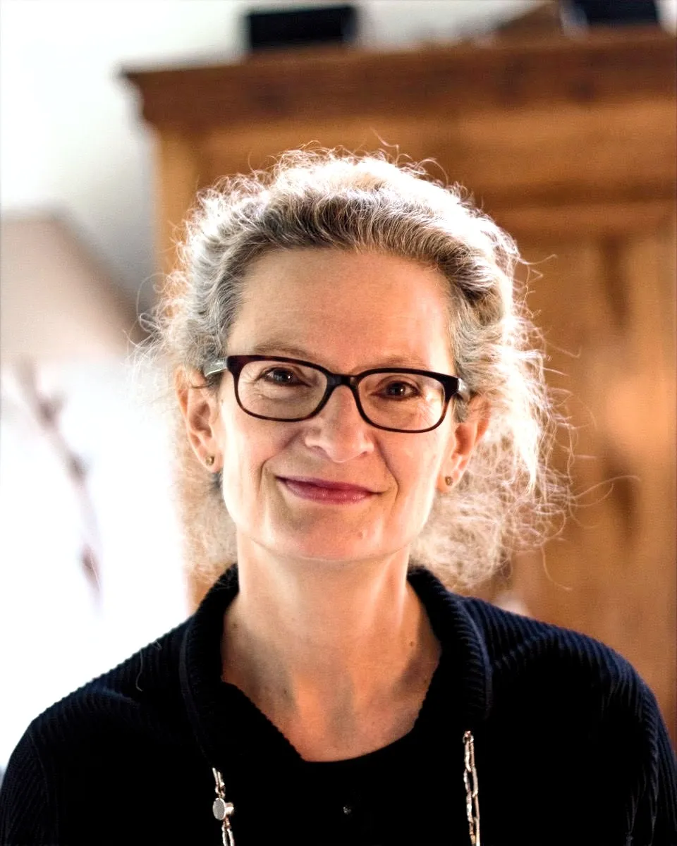 Anne-Claude Benhamiche, psychopraticienne, en portrait, regard chaleureux, fond d'intérieur boisé.